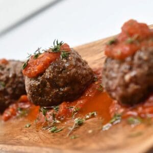 Three meatballs with sauce on a wooden plate.