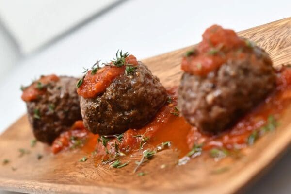 Three meatballs with sauce on a wooden plate.