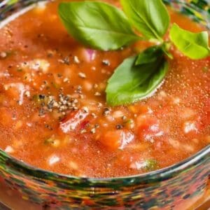 Tomato soup in a glass with basil leaves.