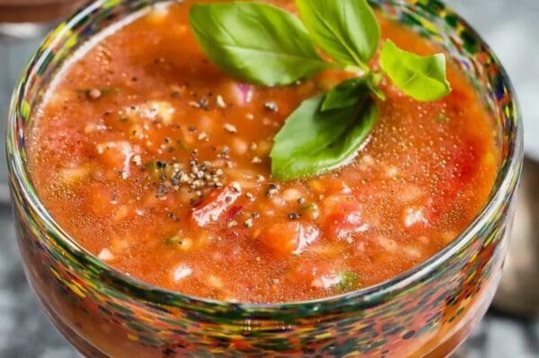 Tomato soup in a glass with basil leaves.