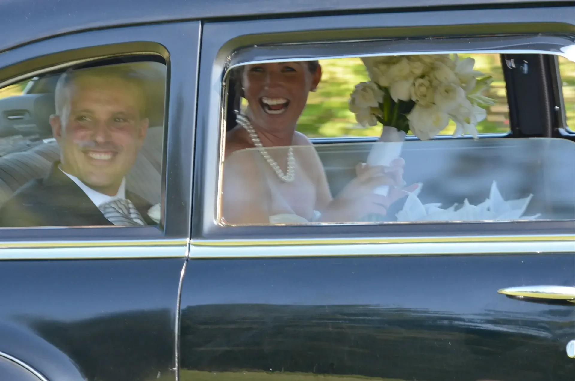 A newly married couple, seated in a car, is being chauffeured away after their wedding ceremony.