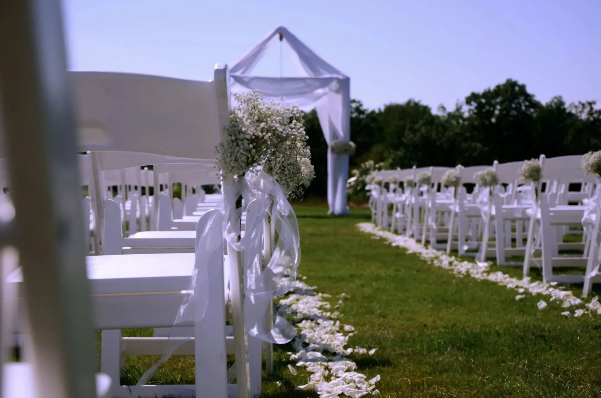 White chairs are set up for an outdoor wedding ceremony with the assistance of offsite catering services.