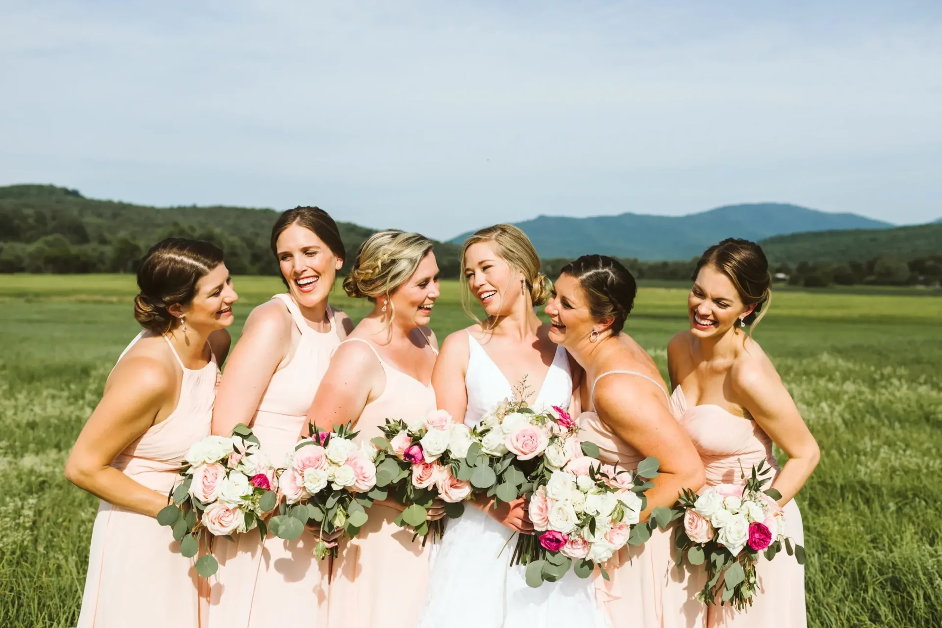 Bridesmaids laughing in a field with mountains and offsite catering services in the background.