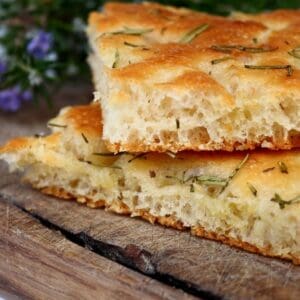 A slice of House Made Focaccia (daily) with rosemary and thyme on a cutting board.