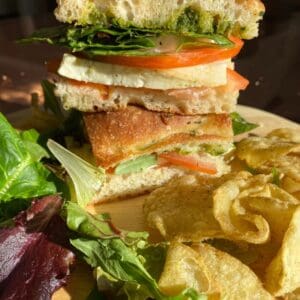 A Caprese on Focaccia on a plate with chips and salad.