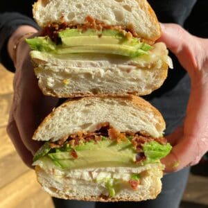 Two people holding up The Waterside Sandwich with avocado and chicken.