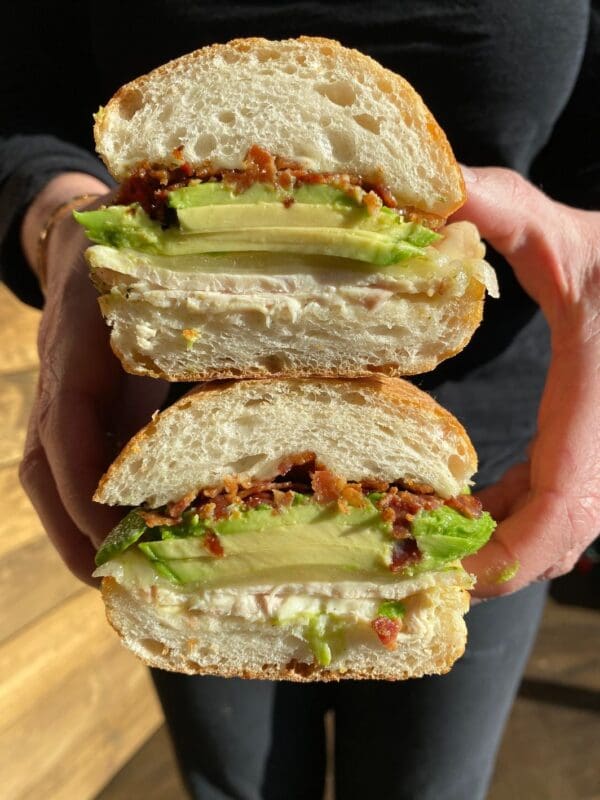 Two people holding up The Waterside Sandwich with avocado and chicken.