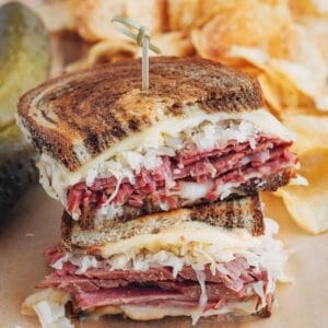 A Reuben sandwich with meat and pickles on a cutting board.