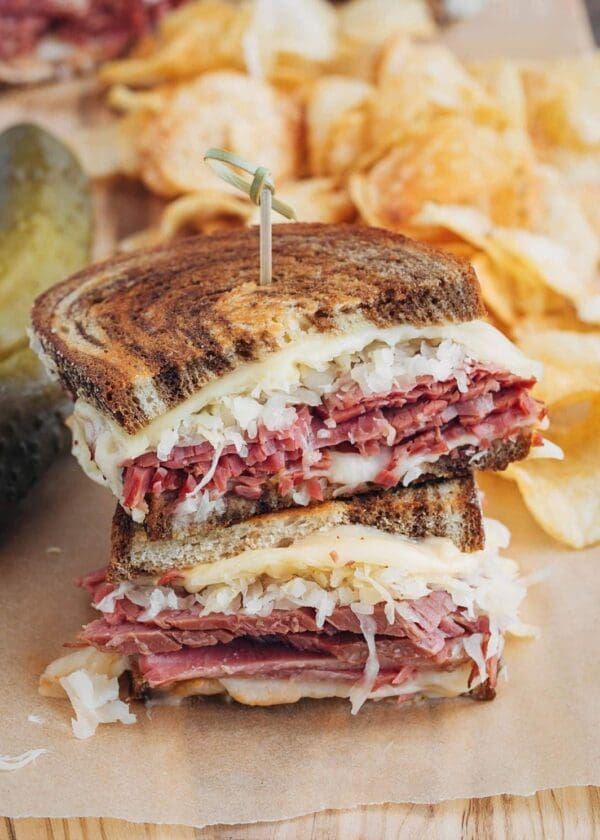 A Reuben sandwich with meat and pickles on a cutting board.