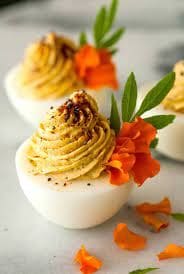 Spicy Chipotle Cage-Free Deviled Eggs with orange flowers on a marble table.