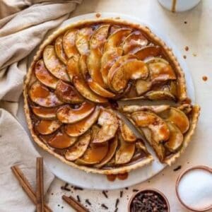 A slice of Fennel-Apple Tarte Tatin on a white plate with cinnamon sticks.