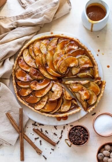 A slice of Fennel-Apple Tarte Tatin on a white plate with cinnamon sticks.