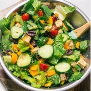 A salad with Arugula & Baby Spinach, tomatoes, cucumbers, and tofu in a bowl.