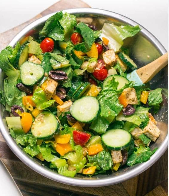 A salad with Arugula & Baby Spinach, tomatoes, cucumbers, and tofu in a bowl.