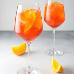 Two glasses of Aperol Spritz Kit for 12 with orange slices in them.