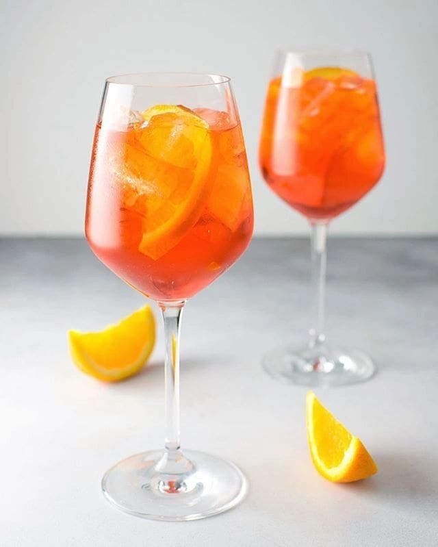 Two glasses of Aperol Spritz Kit for 12 with orange slices in them.