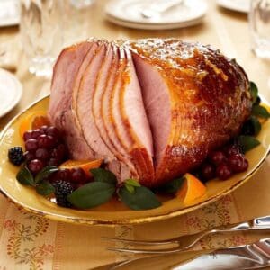 A Dakin Farm Ham is sitting on a plate with fruit and forks.