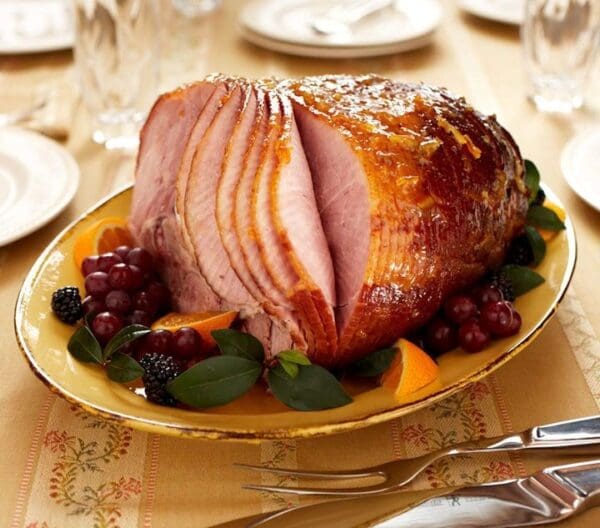 A Dakin Farm Ham is sitting on a plate with fruit and forks.