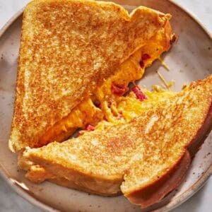 A Pimento Cheese on sourdough sandwich is cut in half on a plate.