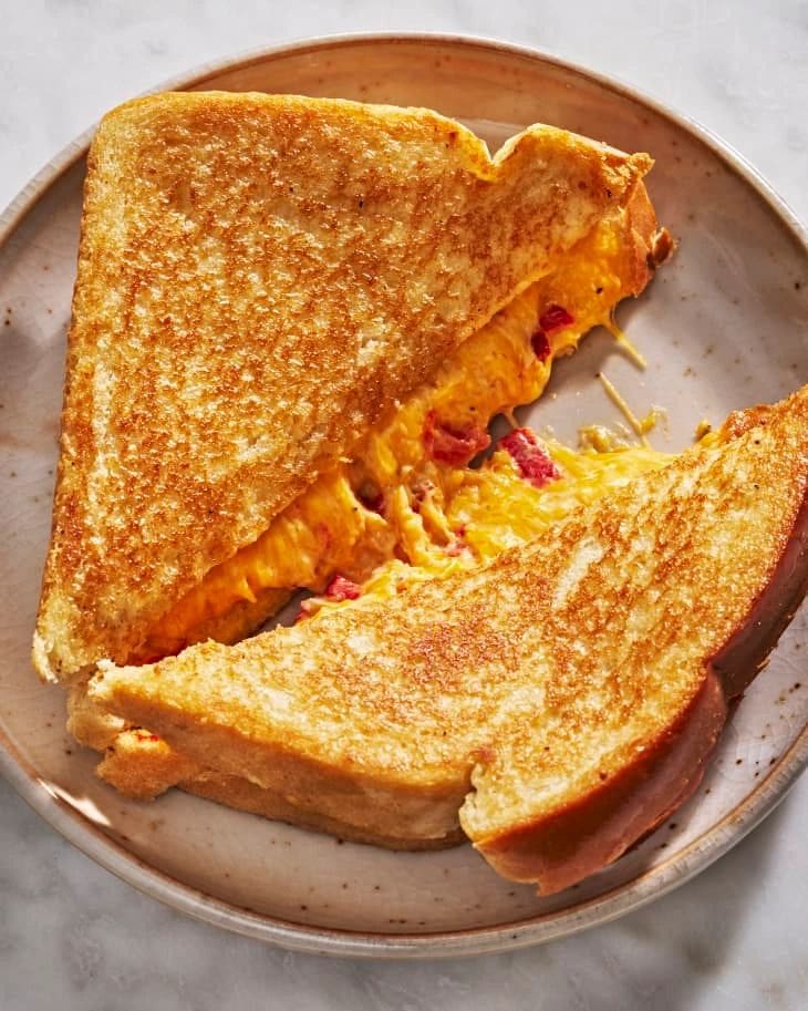 A Pimento Cheese on sourdough sandwich is cut in half on a plate.