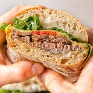 A person holding a sandwich with The Roast and vegetables.