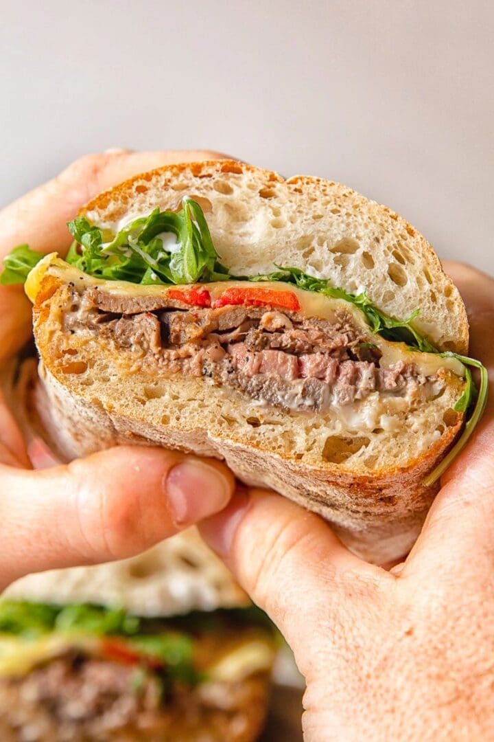 A person holding a sandwich with The Roast and vegetables.