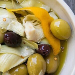 Warm Marinated Olives & Artichokes and oranges in a bowl on a wooden table.