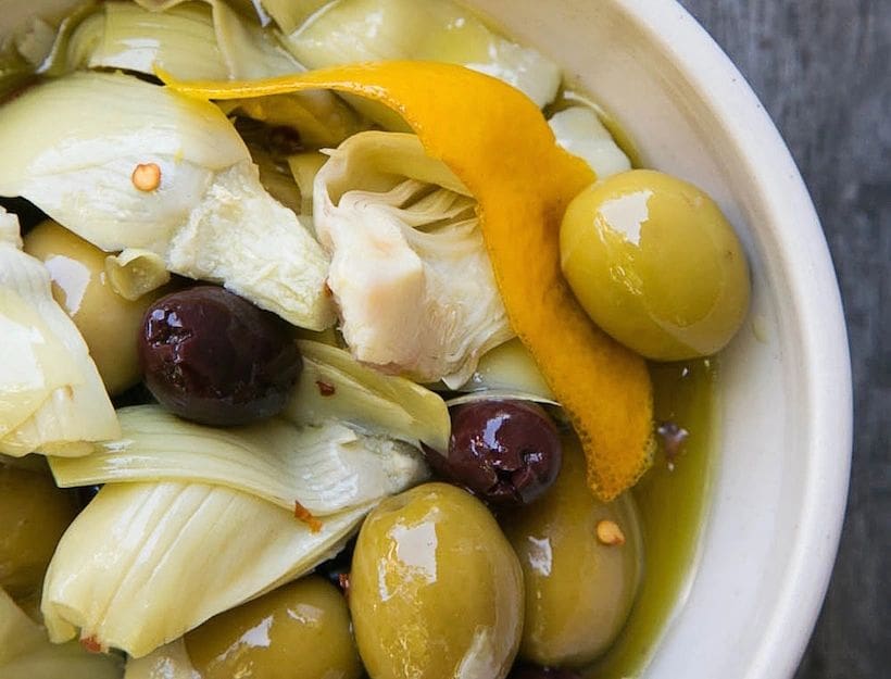 Warm Marinated Olives & Artichokes and oranges in a bowl on a wooden table.